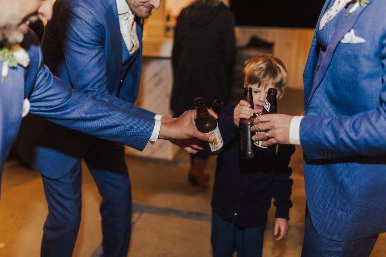 Child holding bottles, handed by men in blue suits, possibly at a wedding.