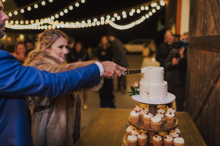 Couple cutting wedding cake outside, evening, string lights.