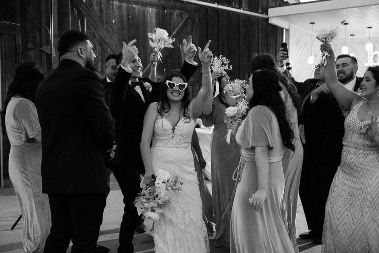 Wedding reception: Bride dances, guests raise hands with bouquets. Black and white, indoors.