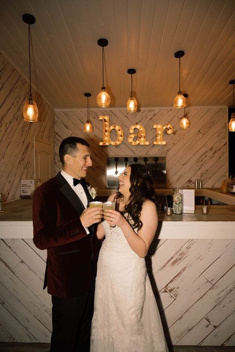 Newlyweds toasting at a bar; couple smiling, holding cocktails. 