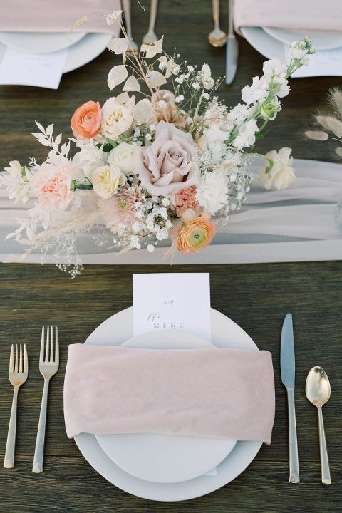 Elegant table setting with floral centerpiece and pink accents on a dark wooden table.