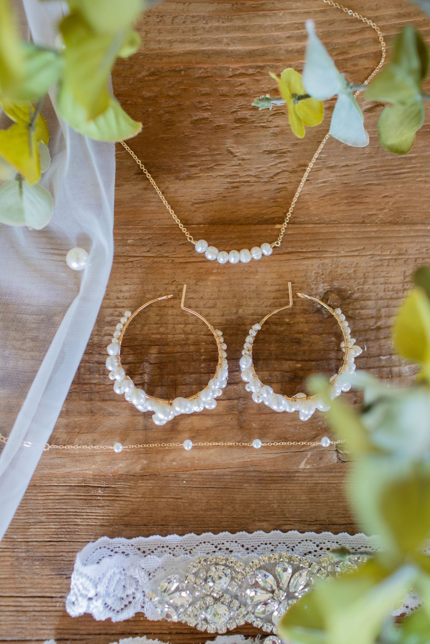 Jewelry set on wood: gold necklace, earrings, bracelet, and garter, with pearls.