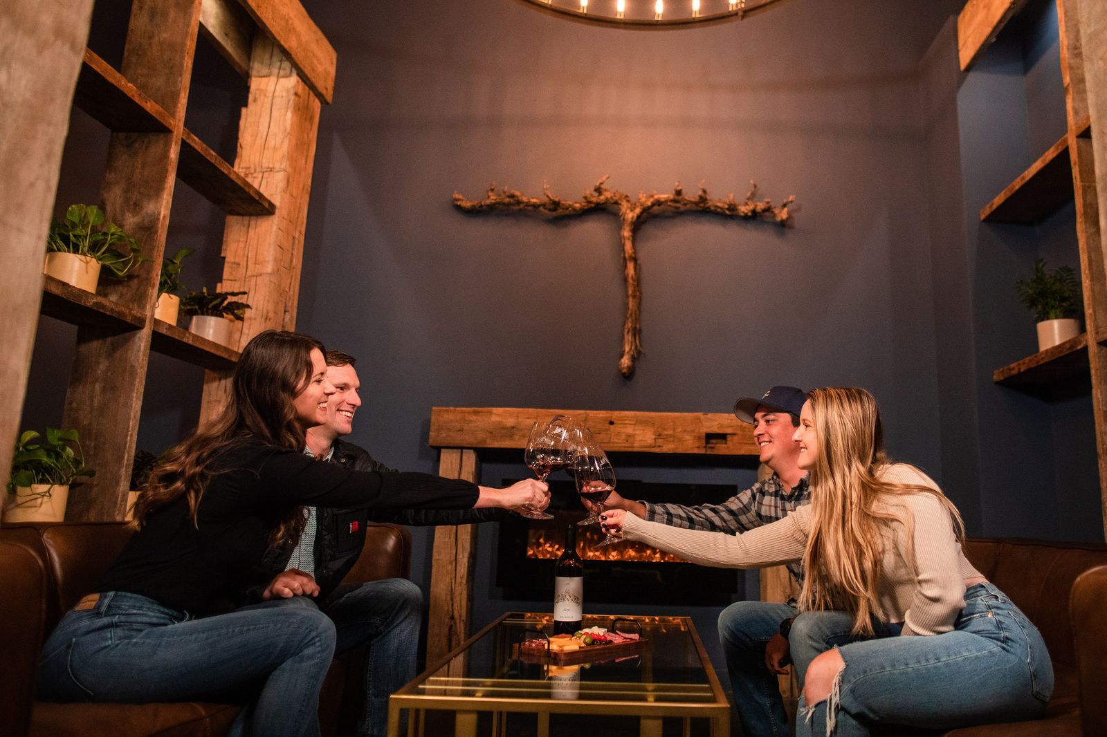 Four people toasting drinks in a dimly lit, wood-paneled room.  They sit on couches near a small table.
