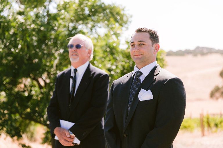 Two men in suits outdoors; one wearing sunglasses, the other with a patterned tie; possibly a wedding ceremony.