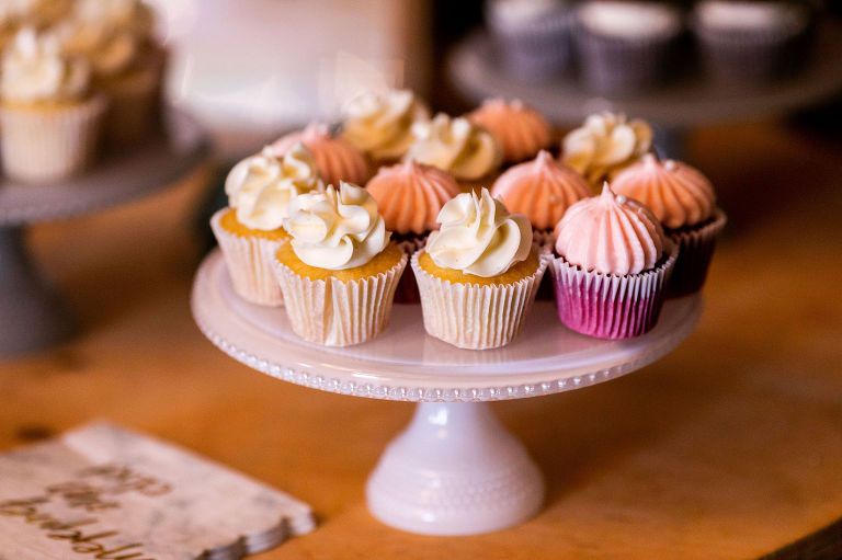 Cupcakes on a white pedestal, with white and pink frosting. Other cupcakes in the background.
