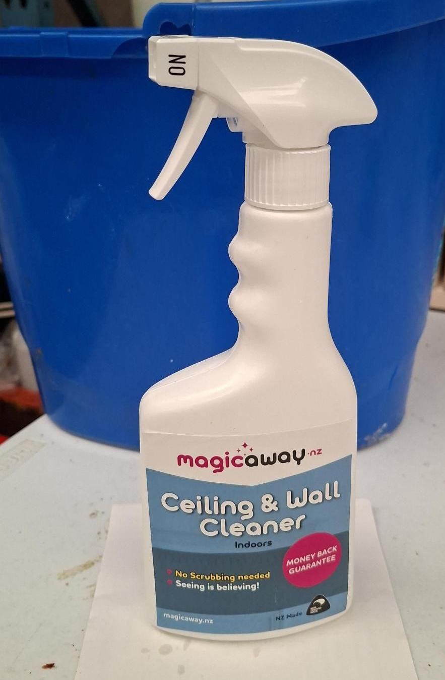 Person wearing blue gloves cleaning a white wall with a cloth spray bottle