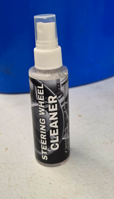 Hands cleaning a car steering wheel and dashboard with orange cloths and spray cleaner