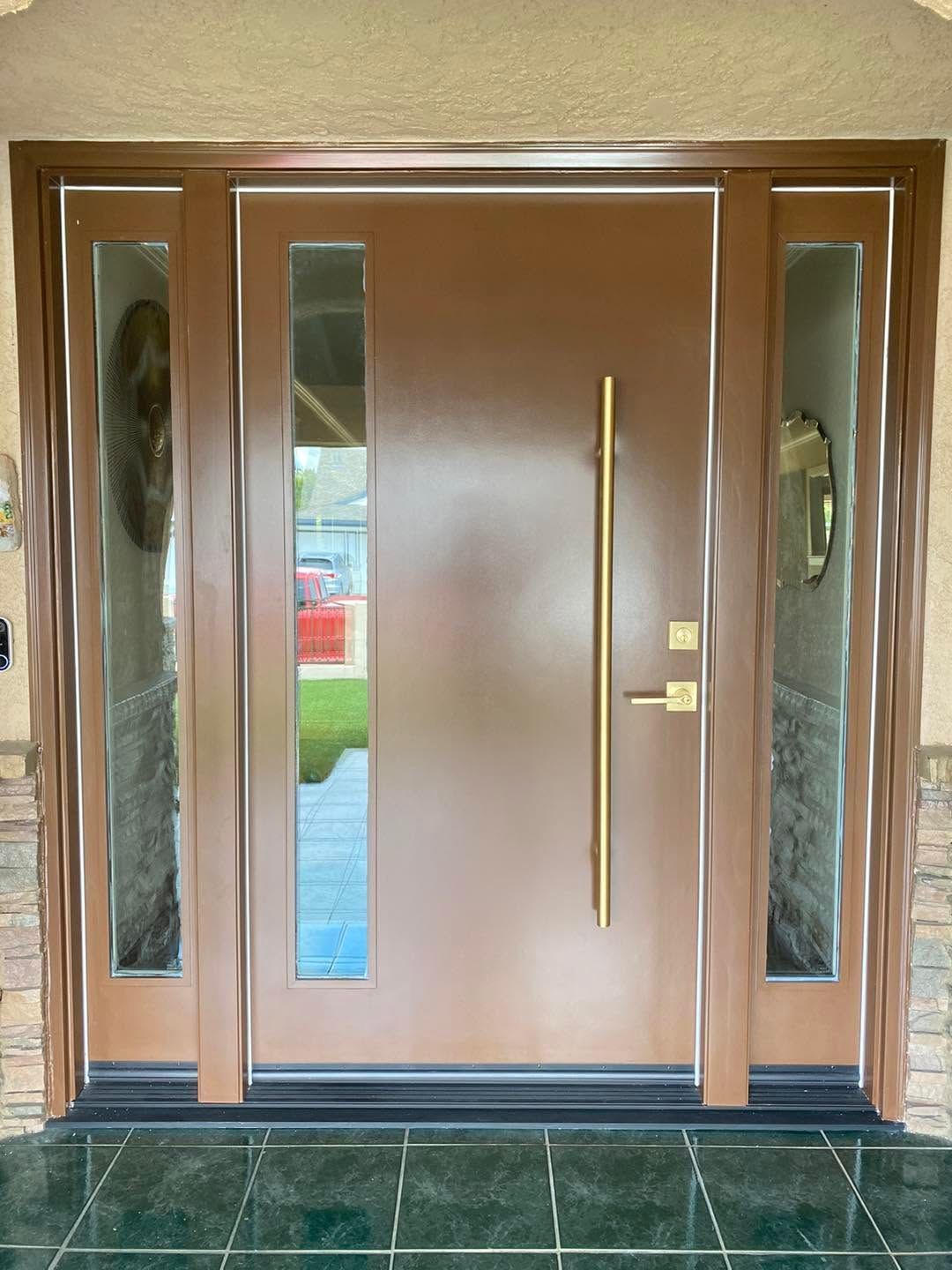 Brown front door with narrow side windows and gold handle, viewed from a tiled entryway
