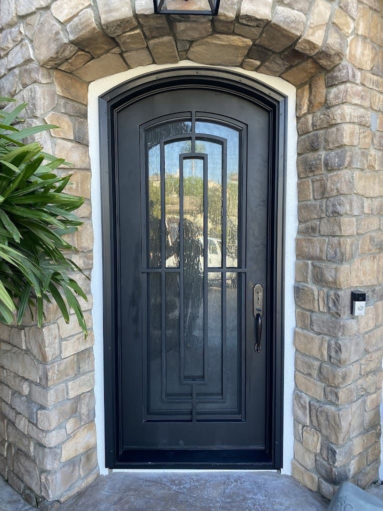 Black arched front door set in a stone entryway with a wrought-iron security grille.