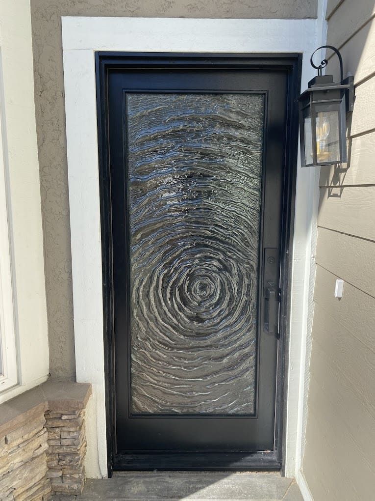 Black front door with frosted glass panel and wall lantern outside a home entrance