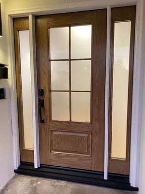 Wooden front door with frosted glass panels and dark trim in a white entryway