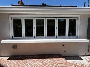 White exterior wall with a row of windows and a narrow awning above a brick patio