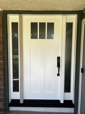 White front door with narrow sidelights and black hardware under a small porch