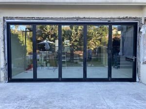 Glass storefront with black-framed sliding doors reflecting trees outside