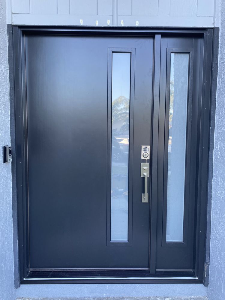 Black front door with narrow vertical glass panels and silver handle in a light blue exterior wall