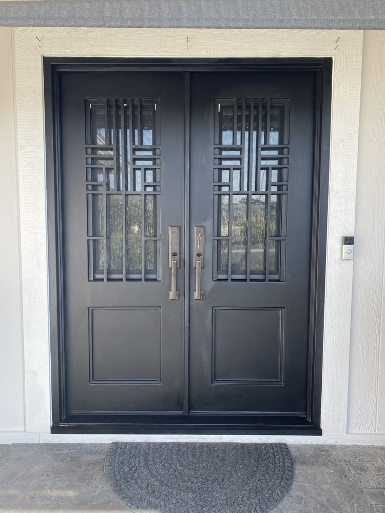 Black double front doors with decorative glass panels and silver handles on a light exterior wall