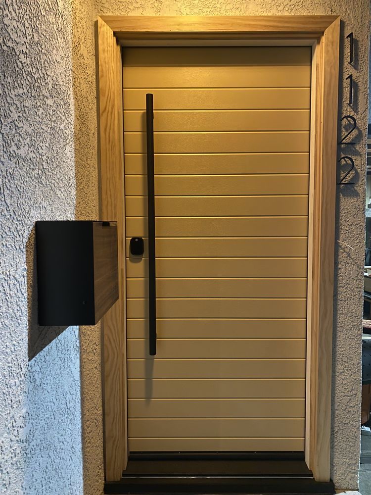 Front door with beige horizontal panels, a long black handle, and a wall-mounted mailbox beside it.