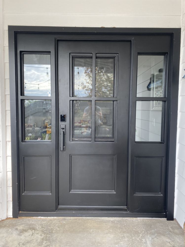 Black double front doors with glass panes and sidelights in a white exterior wall
