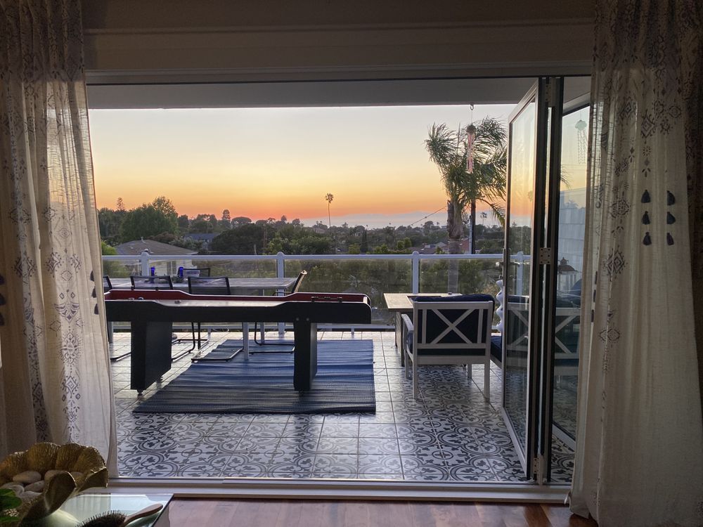 Sunset view from a patio through open sliding doors, with outdoor table and chairs by a pool