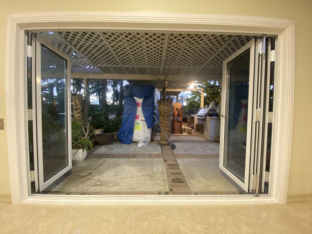 Open white patio doors looking out to a covered patio with a decorative blue-and-yellow sculpture and trees beyond
