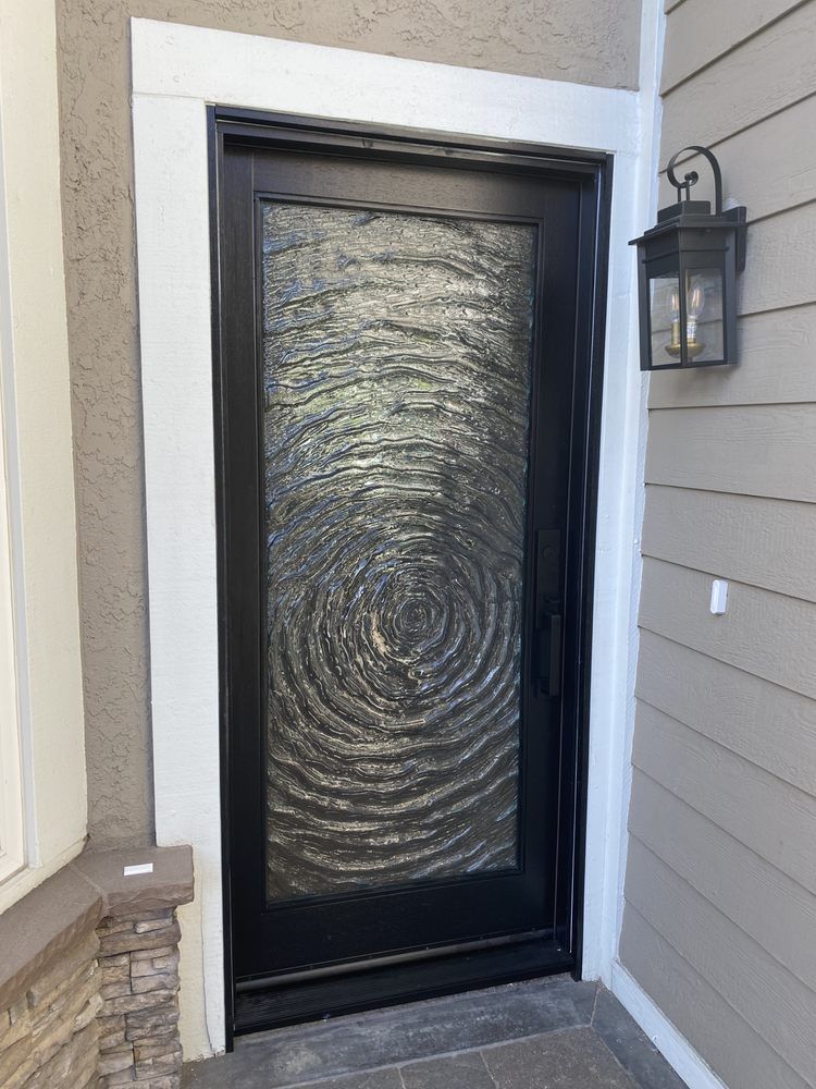 Black front door with textured glass beside stone and siding exterior walls