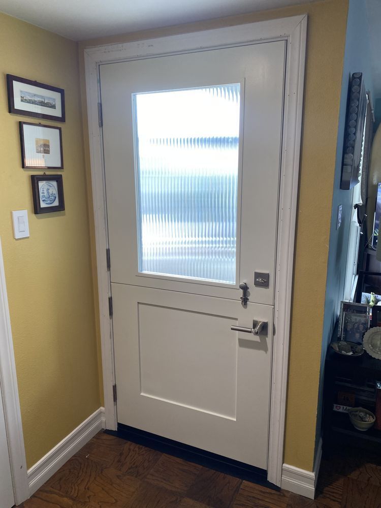 White front door with frosted glass panel in a home entryway, flanked by framed wall art and yellow walls