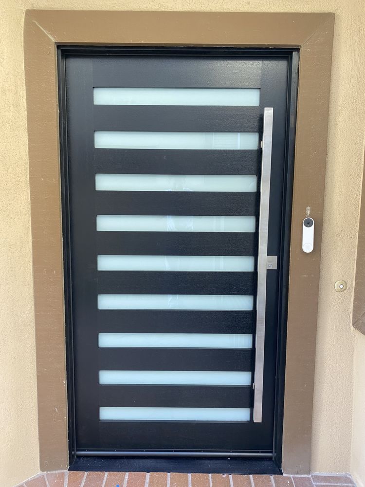 Modern black front door with horizontal frosted glass panels and a white handle, set in a beige wall.