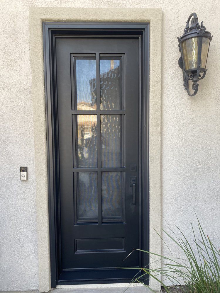 Black front door with glass panels, wall lantern, and beige stucco exterior.