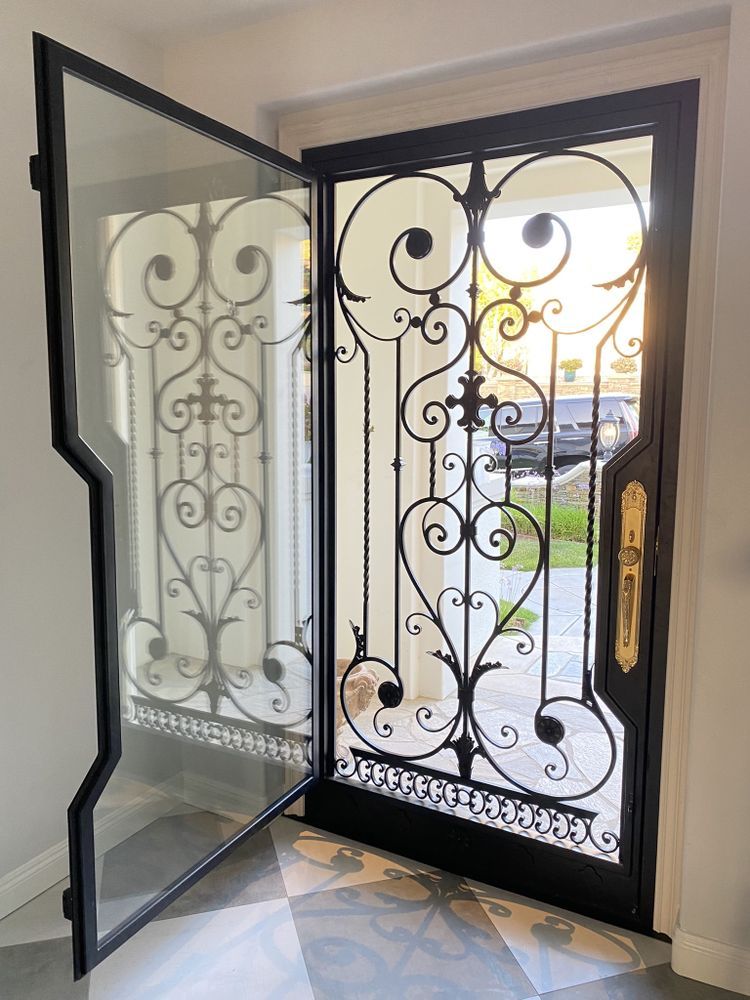 Open black wrought-iron front door with glass panel, leading to a bright entryway and driveway outside