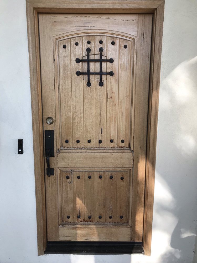 Wooden front door with black iron cross grille and arched top, set in a white stucco wall.