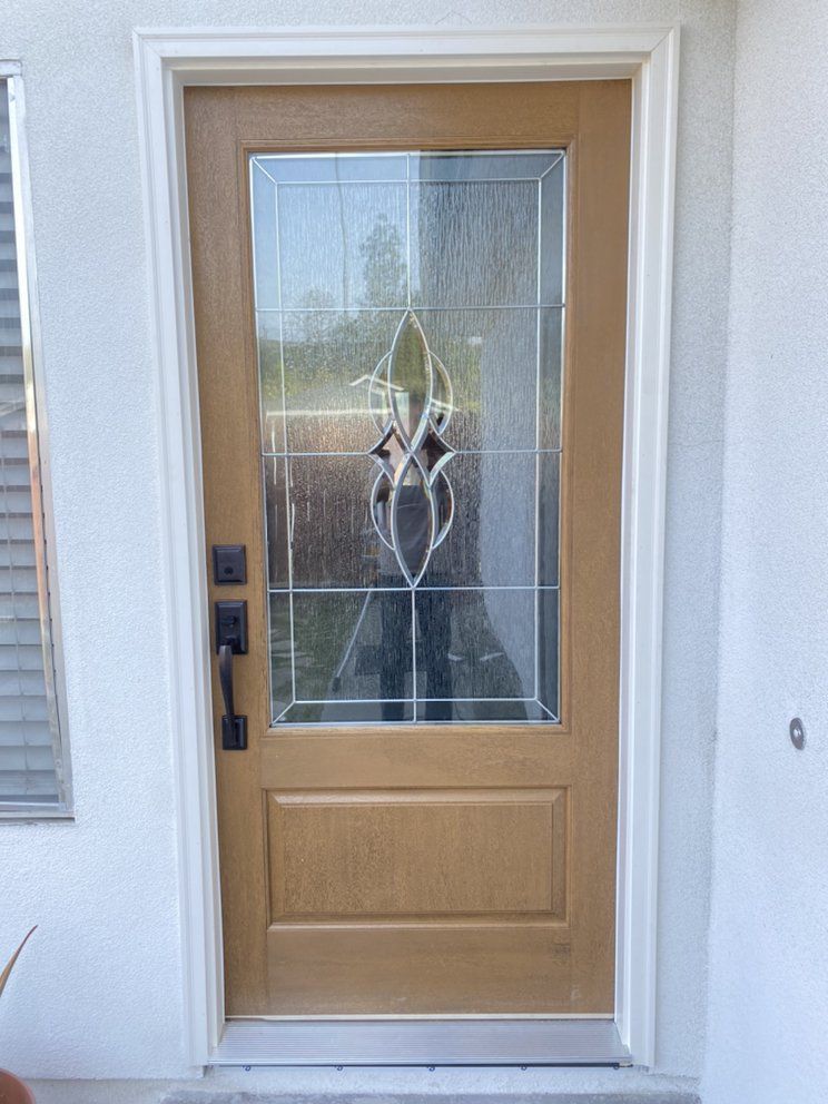 Front door with frosted glass and wood finish, featuring a holiday wreath and white trim.