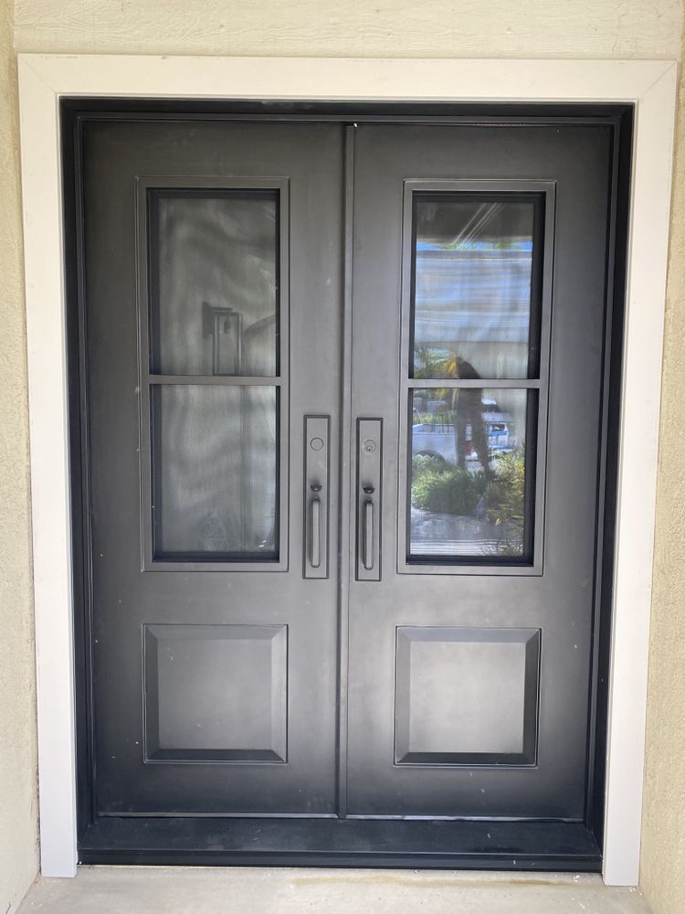 Dark gray double front doors with glass panes and vertical handles at a house entrance