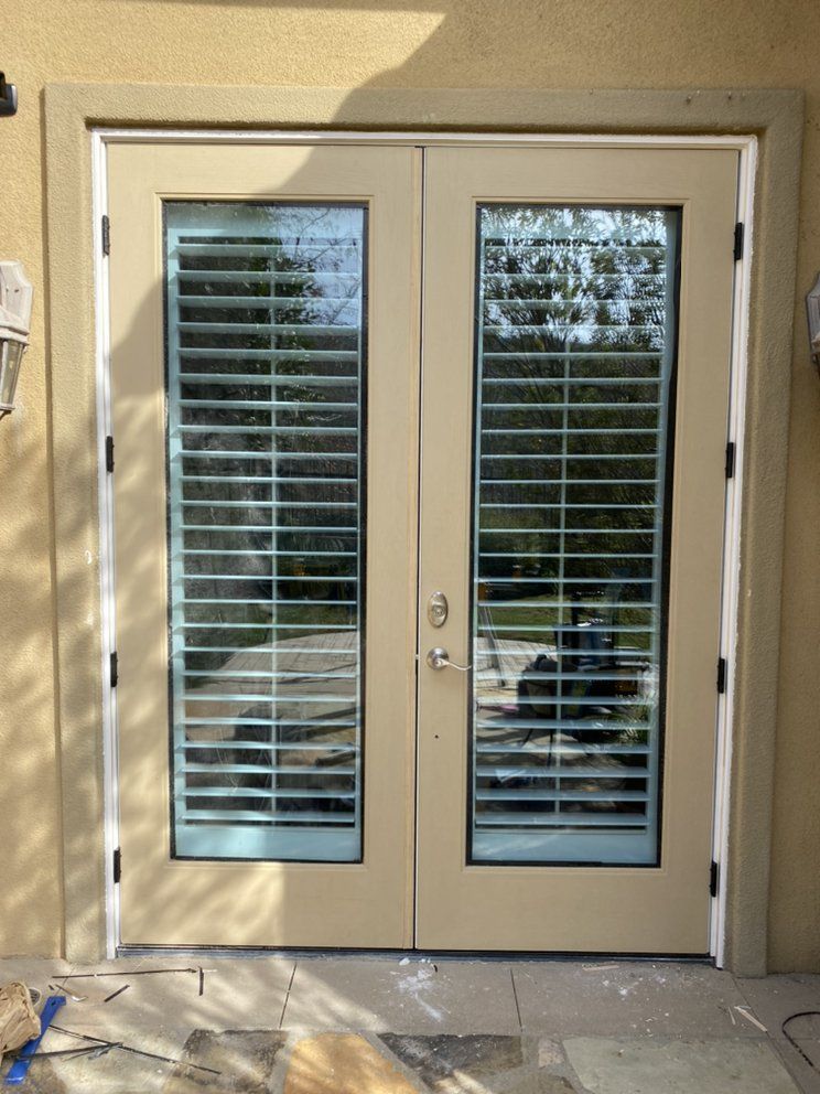 Beige double French doors with narrow glass panes and white blinds on a patio.