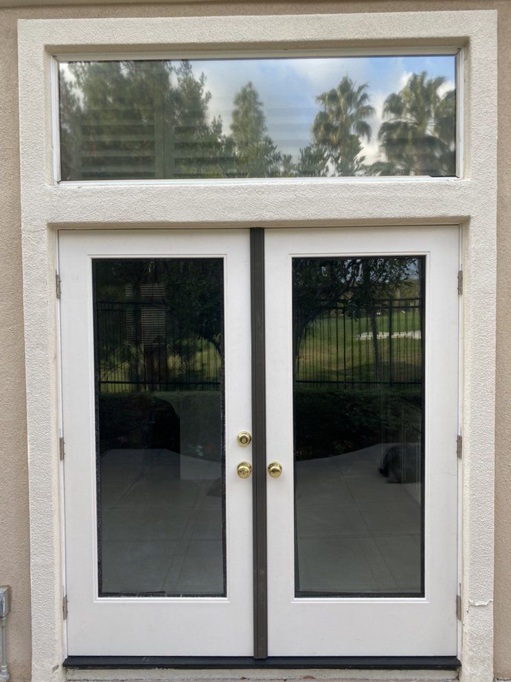 White double glass doors with brass knobs beneath a narrow transom window on a stucco exterior