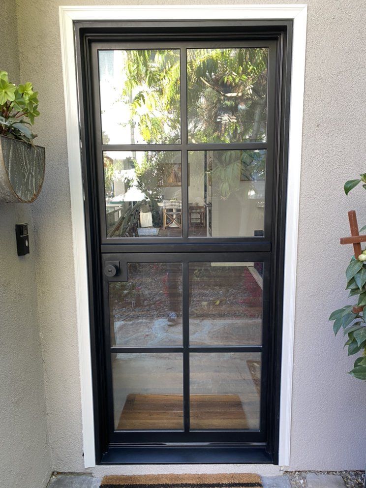 Black-framed glass front door with a window view of a patio and trees outside.
