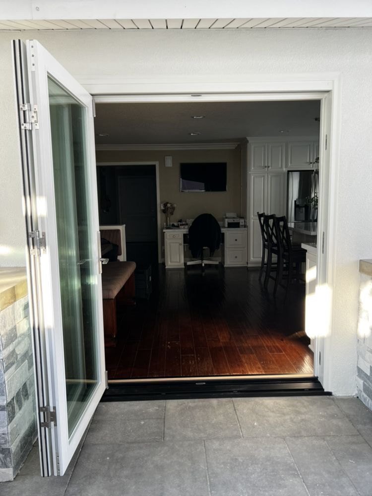 Open folding doors to a dimly lit dining room with dark wood floors and chairs.