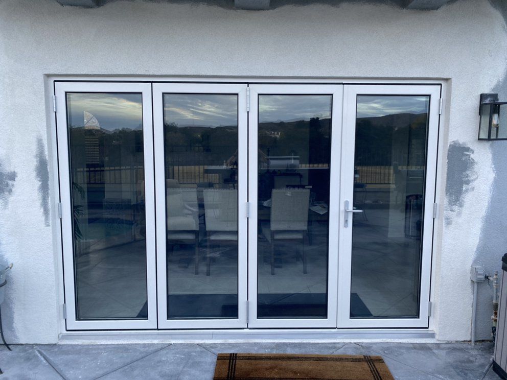 Closed four-panel glass patio doors in a light gray wall with outdoor reflections