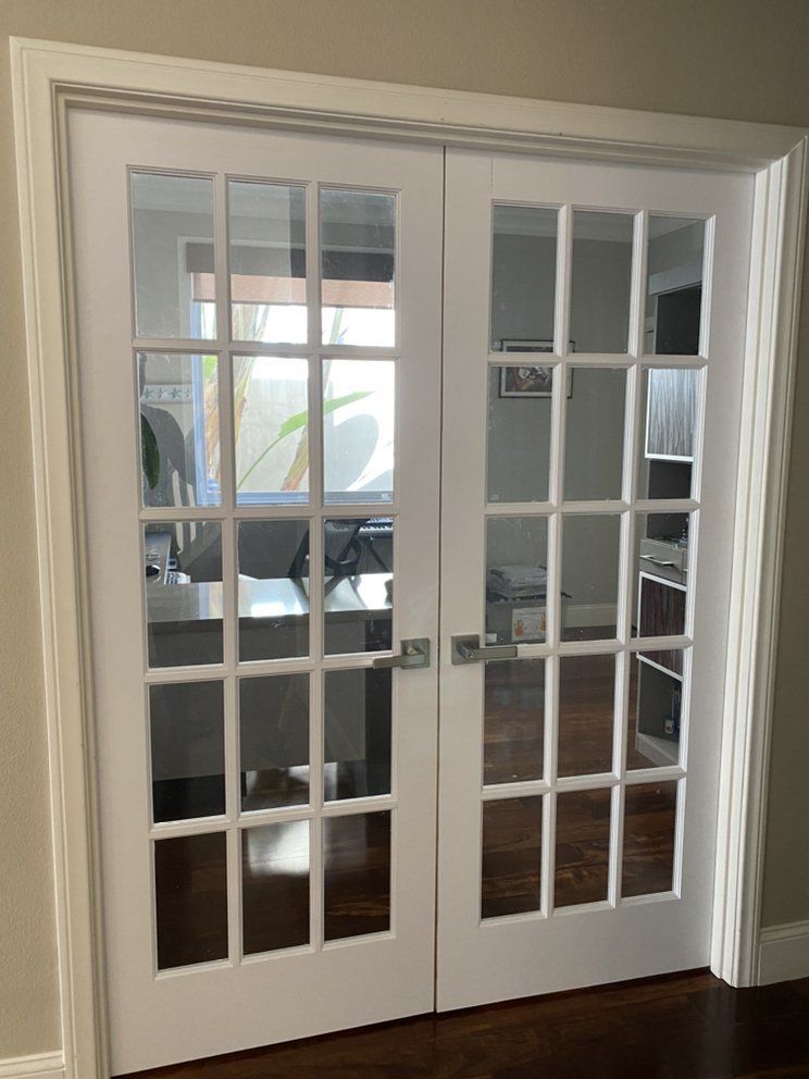 White French doors with multiple glass panes opening into an office with desks and chairs.