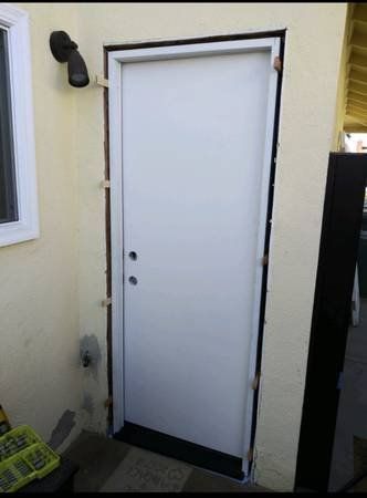 White exterior door framed by dark trim beside a window and wall-mounted light outdoors