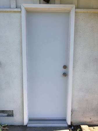Closed white exterior door with two round doorknobs in a stucco wall