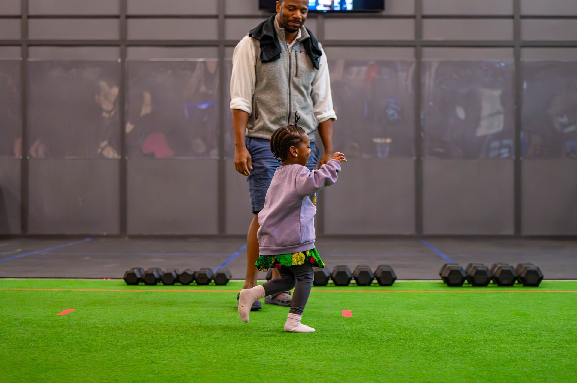 A man and a little girl are walking on a green field.