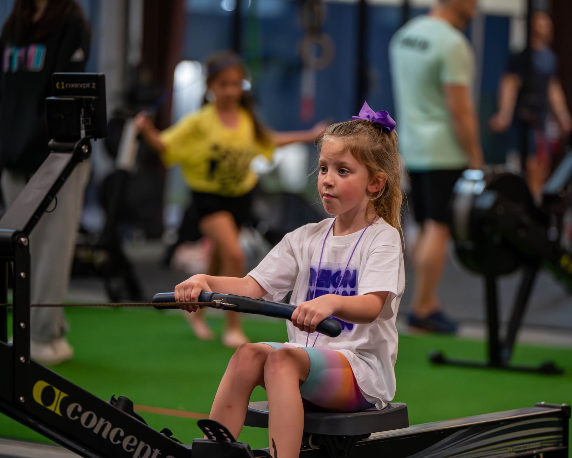 A little girl is sitting on a rowing machine in a gym.