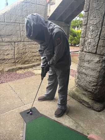 Person practicing golf putting on a wet patio beside stone walls and steps.