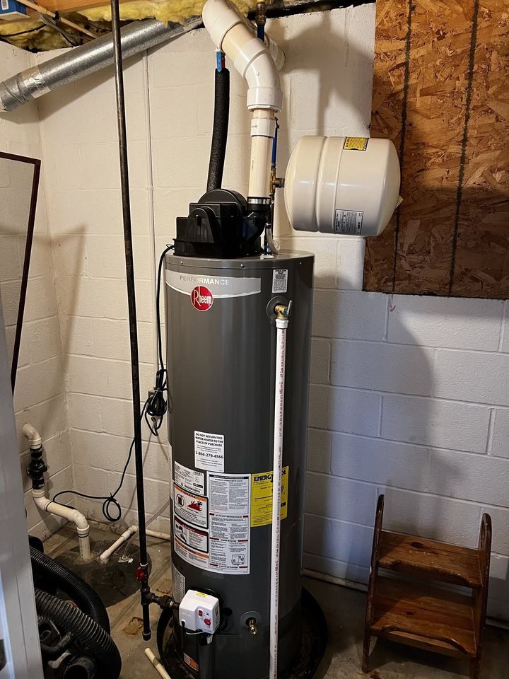 Gas water heater in a basement with white vent pipes and cinder block walls.