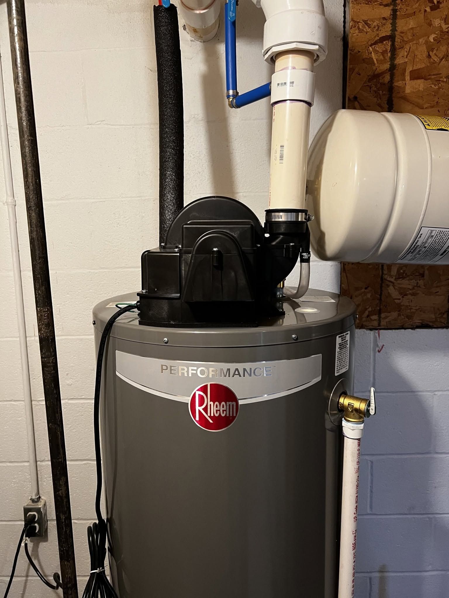 Rheem water heater with black vent piping in a utility room against white walls