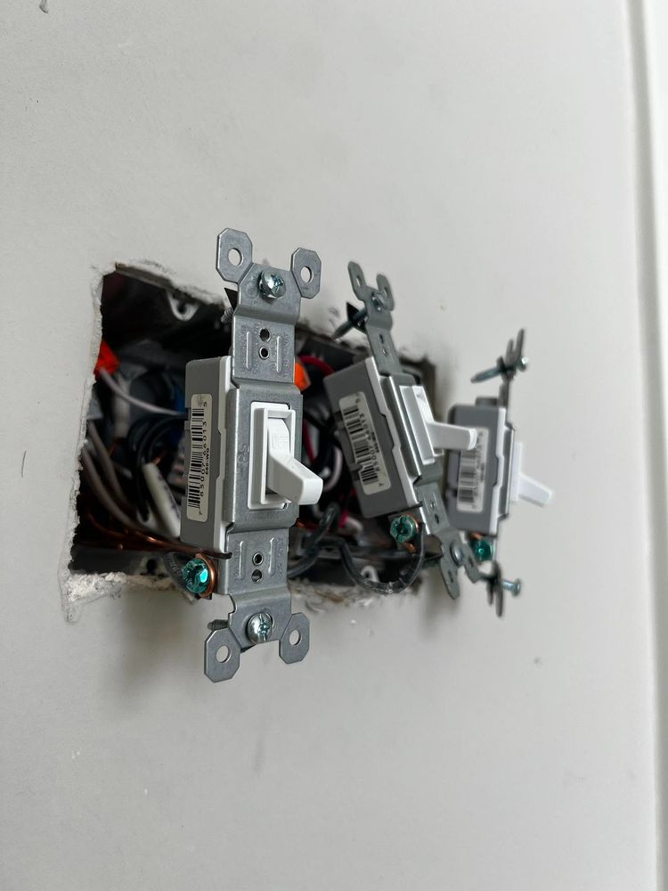 Two wall switches mounted in an unfinished electrical box with exposed wires