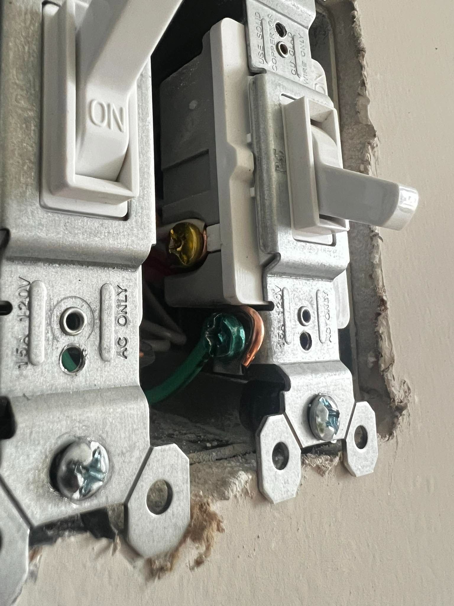 Close-up of an open electrical wall switch with exposed wires and screws in a wall outlet box.