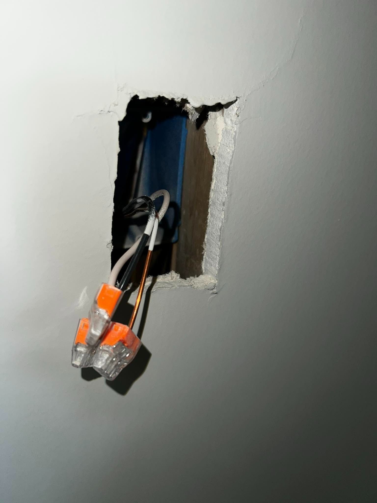 Exposed electrical wires with orange wire nuts protruding from a rough wall opening