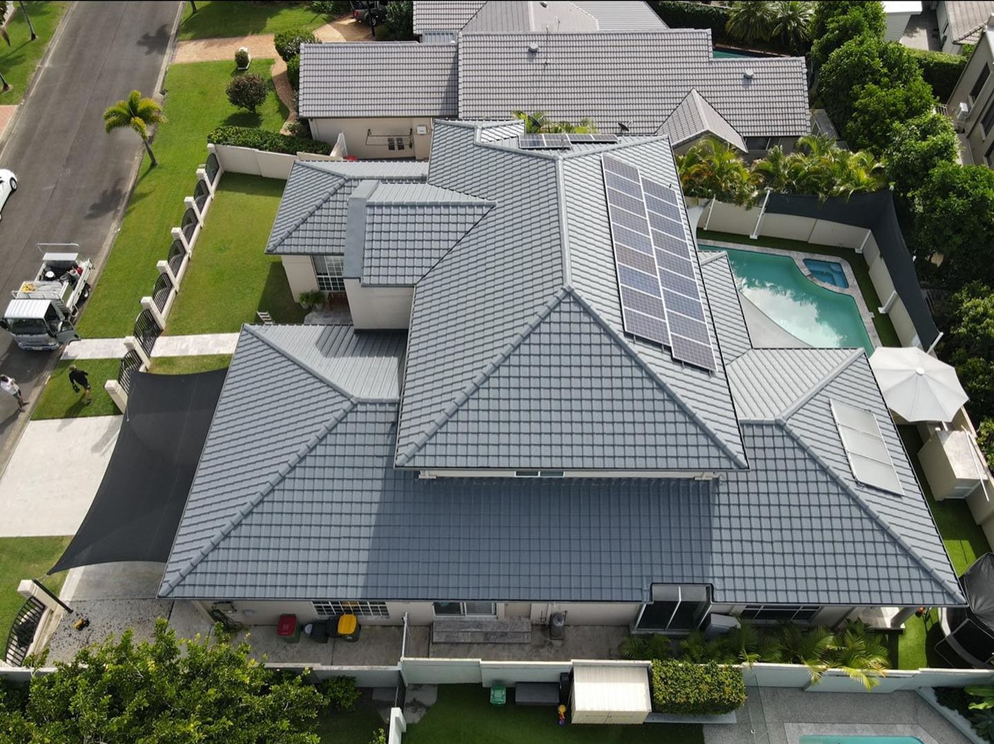 Overhead view of a house with a gray tile roof, solar panels, and a swimming pool in a suburban setting. - Roof Painting in Gold Coast,QLD