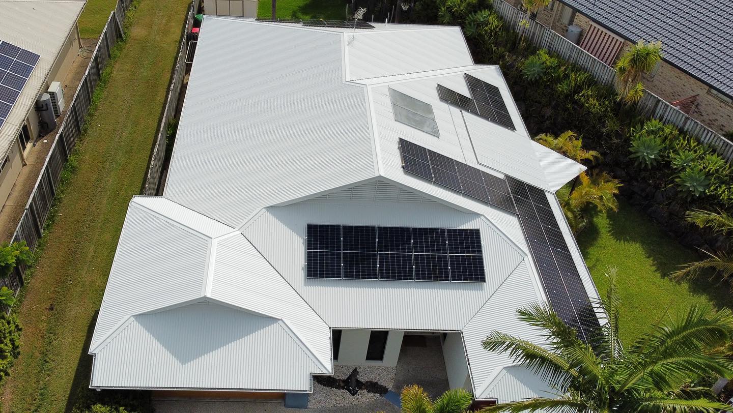 Aerial view of a white house with solar panels on its roof surrounded by green grass and trees. - Roof Painting in Gold Coast,QLD